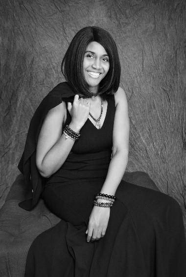 A black and white picture of the author, Lashun Williams, in a fancy black dress and holding a similarly colored jacket behind her.